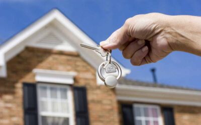 hand holding house keys in front of house