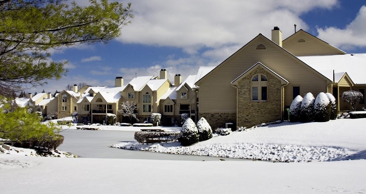 A winter scene featuring snow-covered houses and a serene pond.