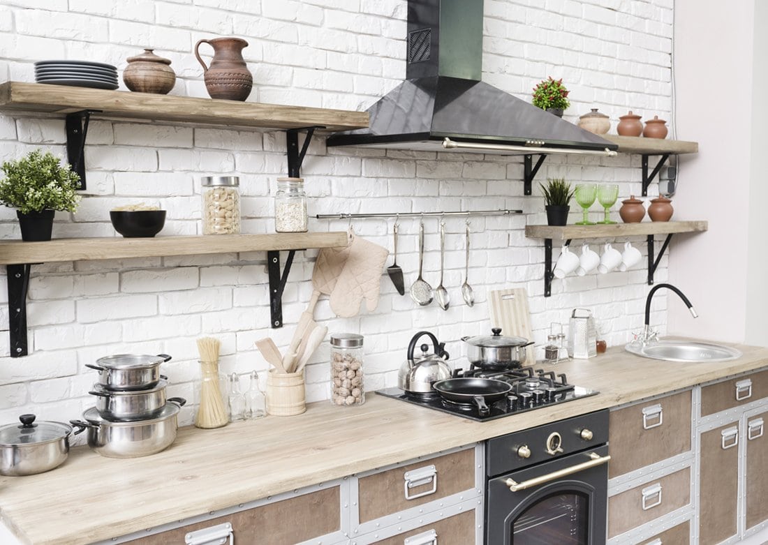 A white kitchen with wooden shelves and pots on the wall.