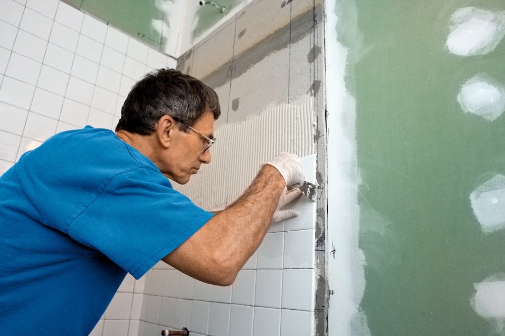 Man applying ceramic tile to a bathtub enclosure wall, how long does it take to remodel a bathroom