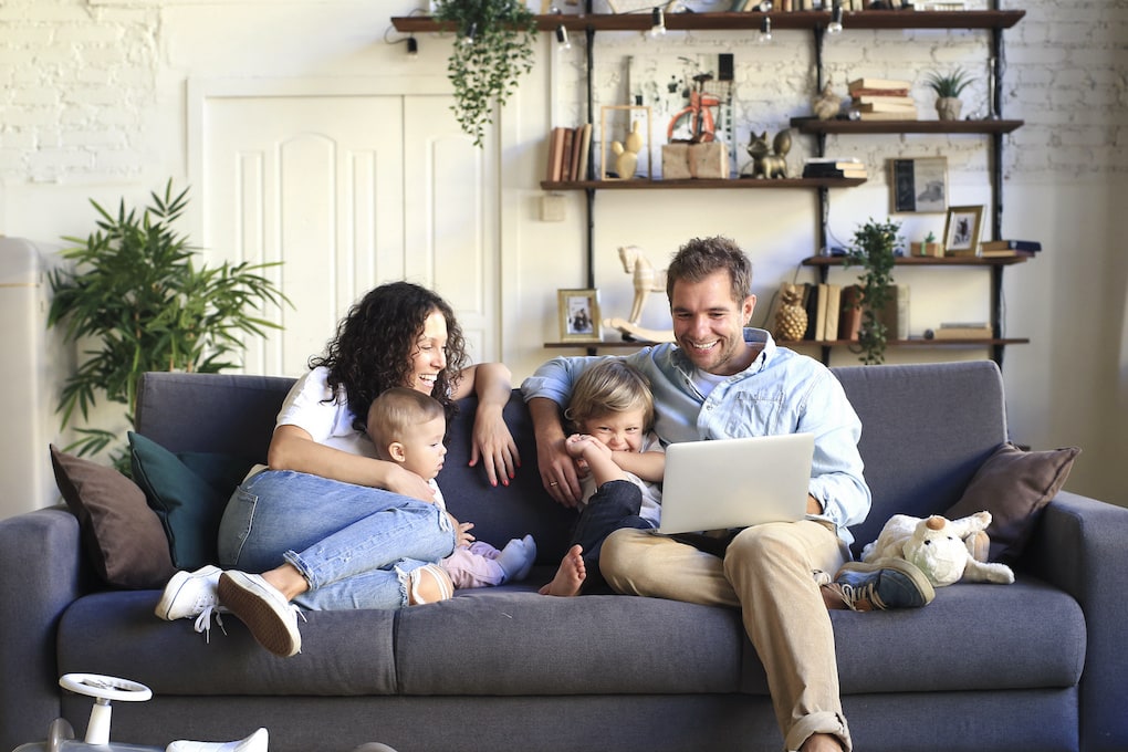 A family is sitting on a couch using a laptop.