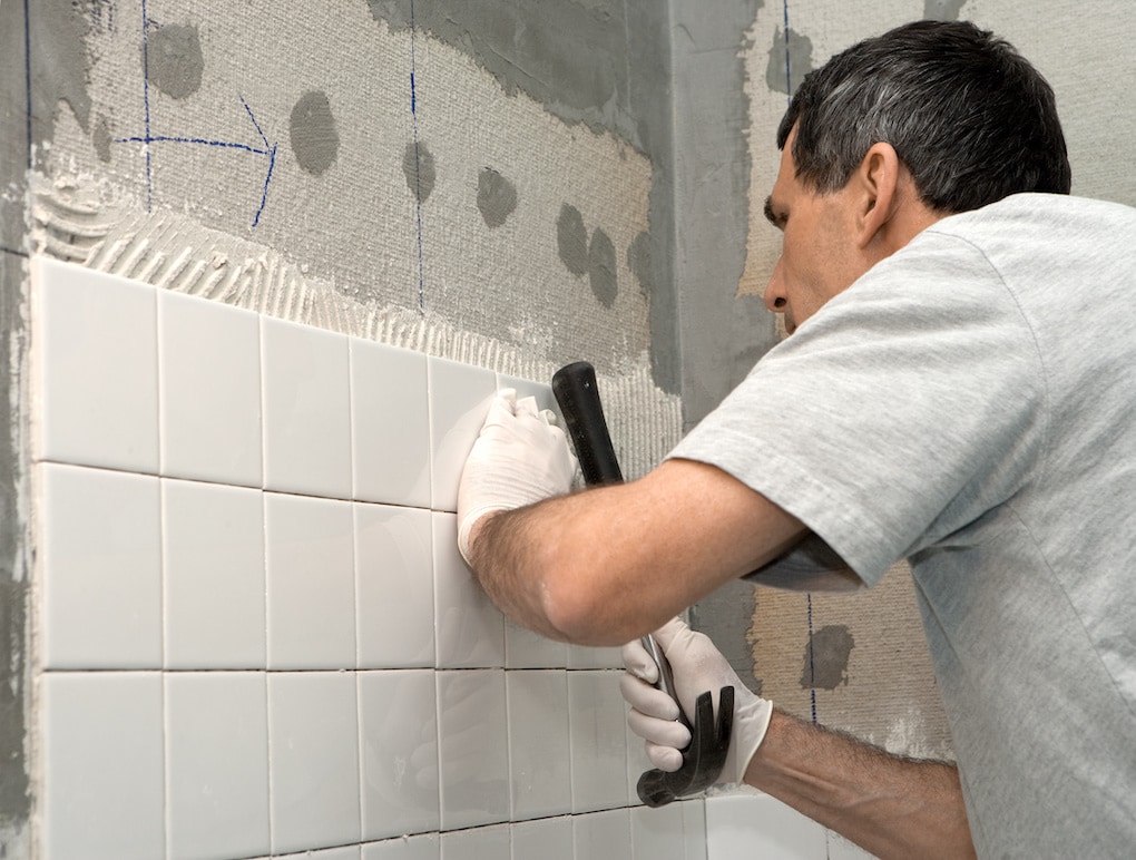 Man setting tile on cement board with diy bathroom remodel tools