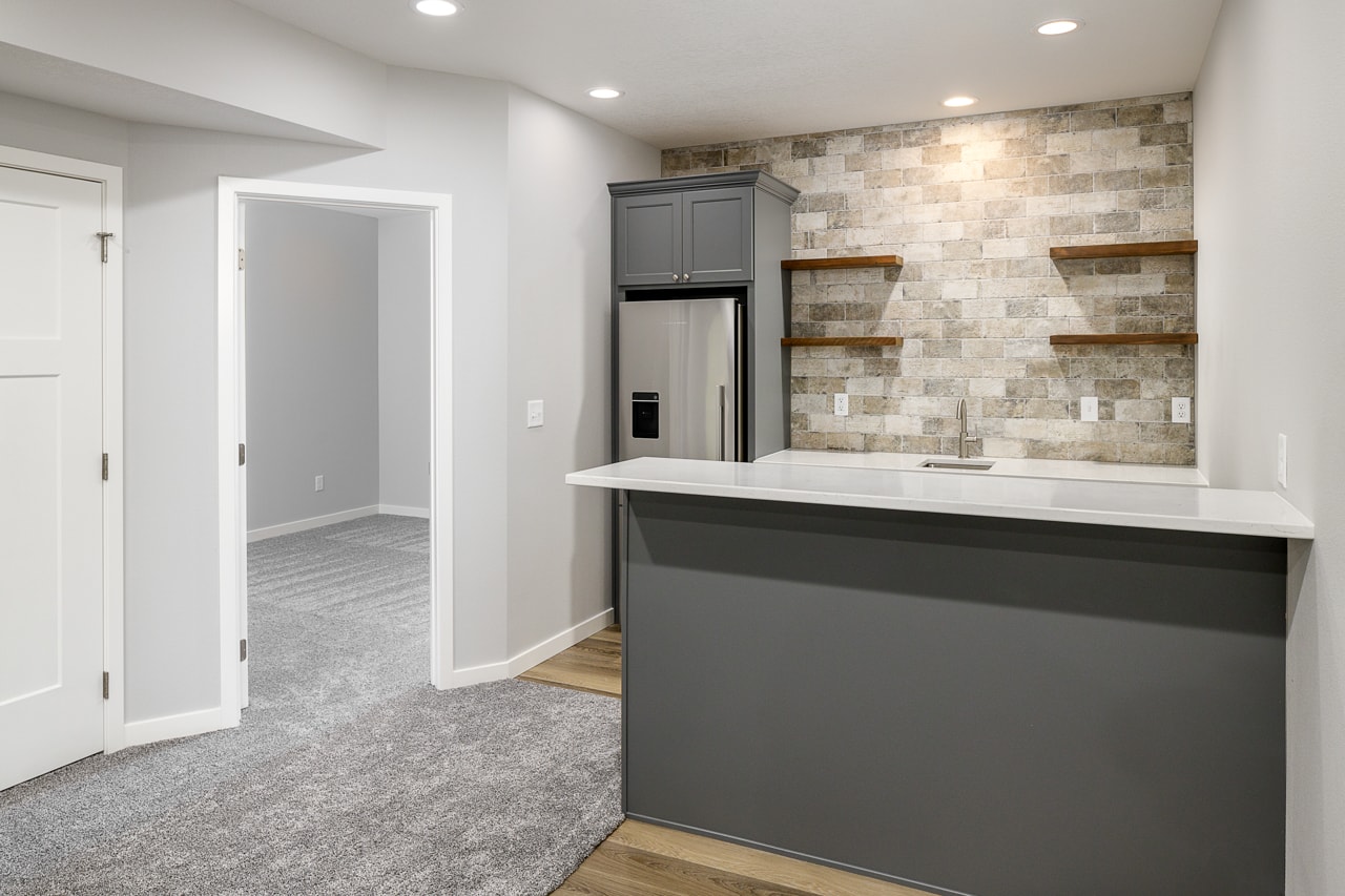 A small kitchenette in a finished basement with a refrigerator and a sink.