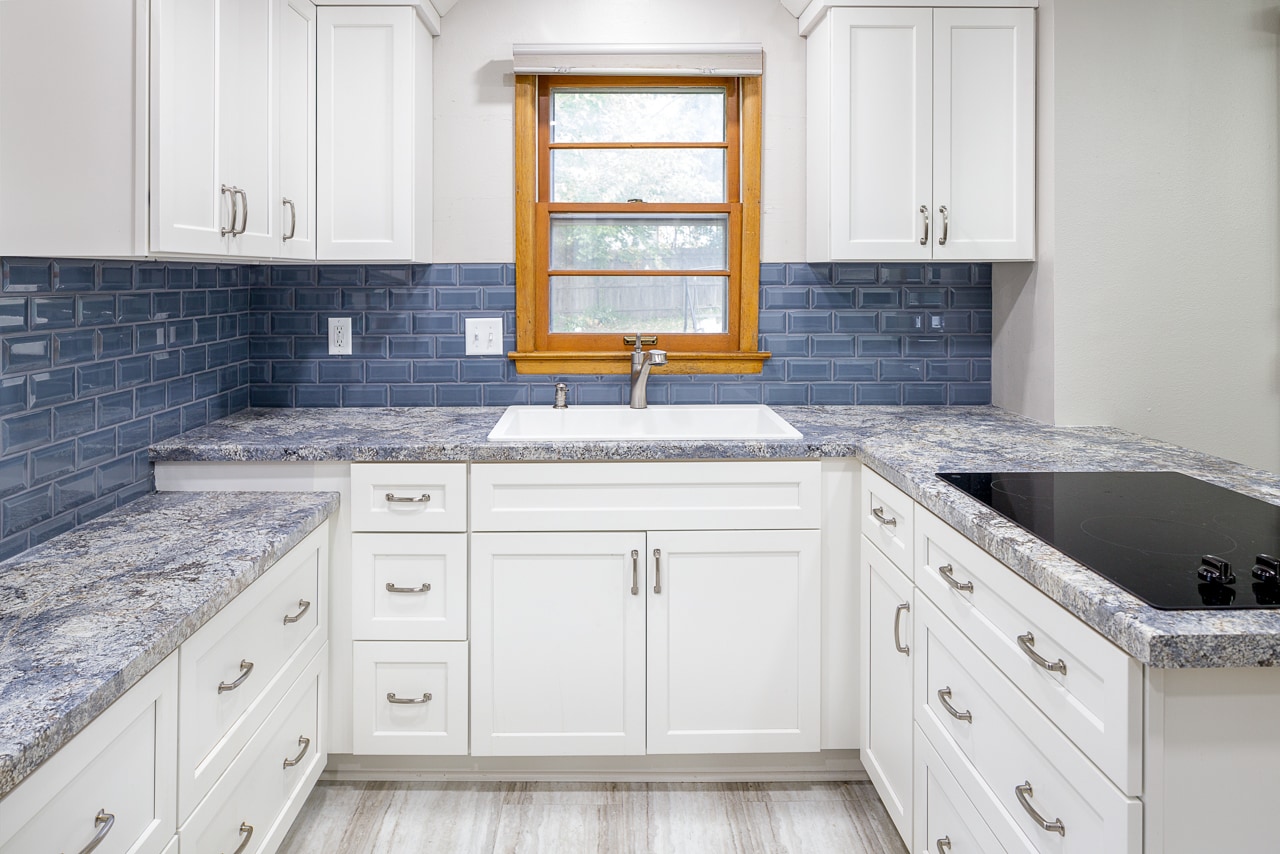 A renovated kitchen with white cabinets and blue tile.